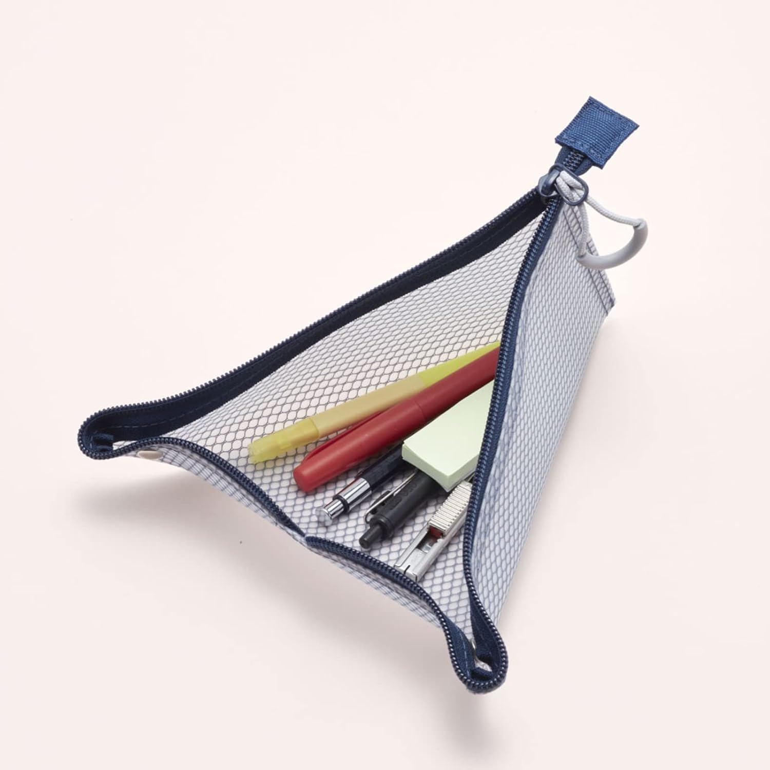 A triangular mesh pencil pouch with a navy blue zipper and trim, shown open with pens and a sticky note inside, on a light beige background.