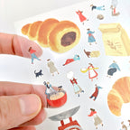 Hand holding sticker sheet with theme of baking with little friends over white background.