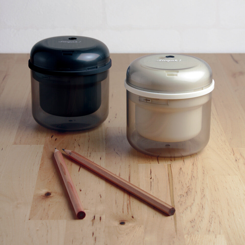 Two cylindric electric sharpener in black and beige and pencils on wooden surface.