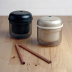 Two cylindric electric sharpener in black and beige and pencils on wooden surface.
