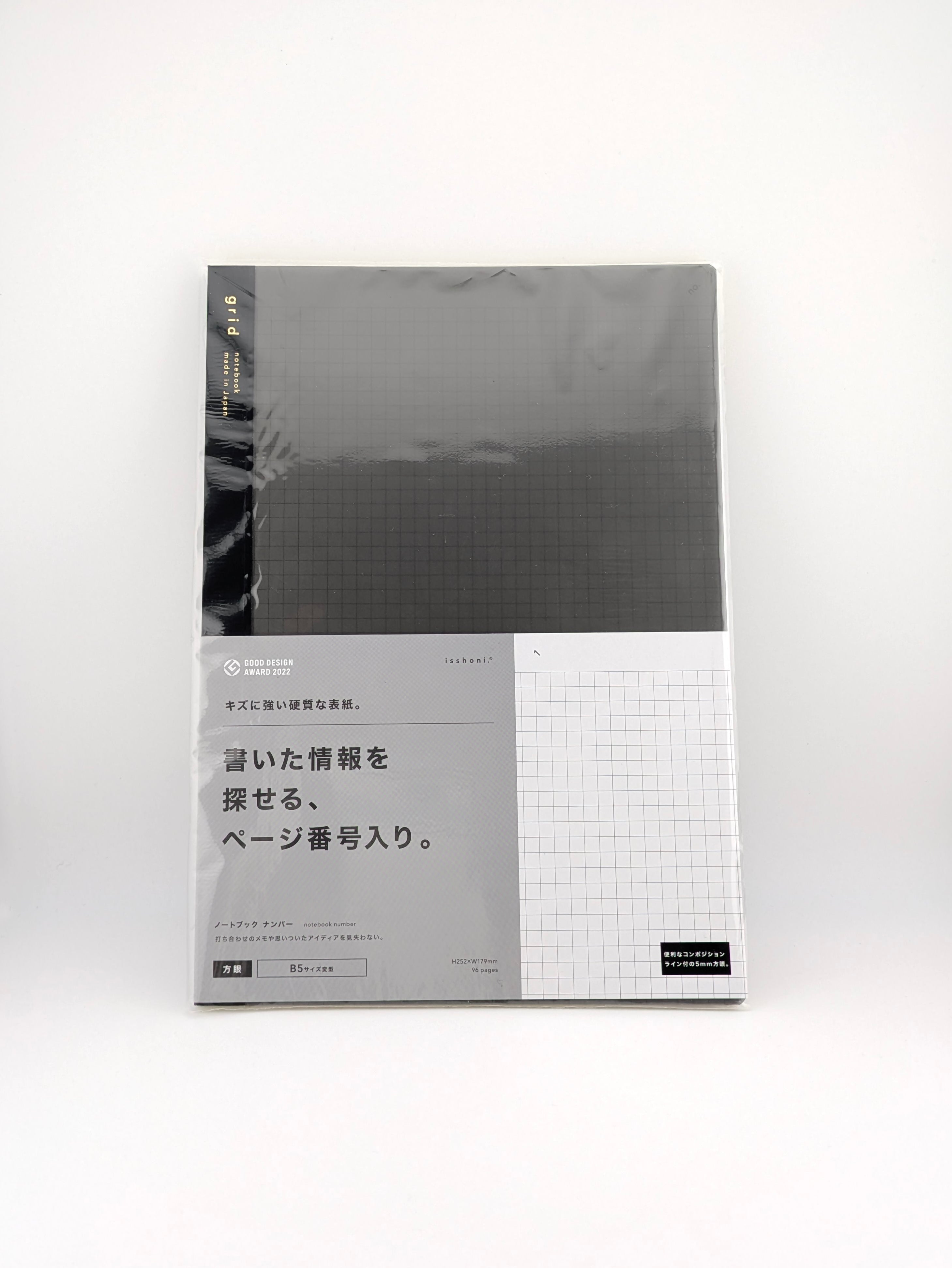 A slim rectangular notebook or journal with a dark charcoal gray cover and a light gray lower section featuring Japanese text and a white grid pattern, photographed on a clean white background.