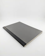 A hardcover notebook or journal with a textured dark gray cover and a black spine, photographed at an angle on a light gray background.