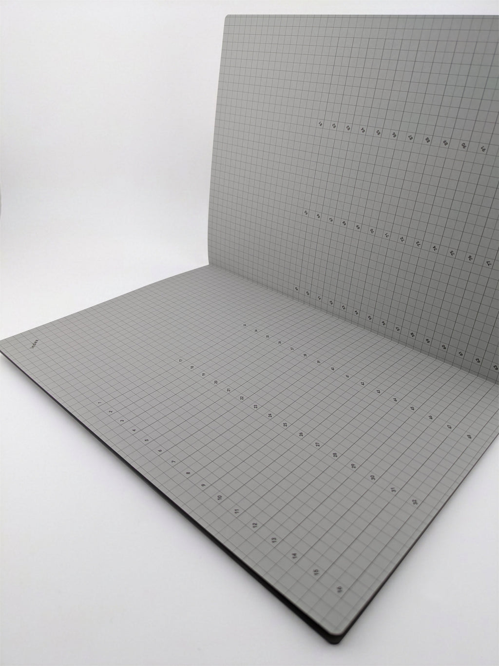 An open notebook or sketchbook with light gray graph paper pages, photographed on a plain white studio background.