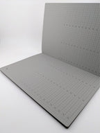 An open notebook or sketchbook with light gray graph paper pages, photographed on a plain white studio background.
