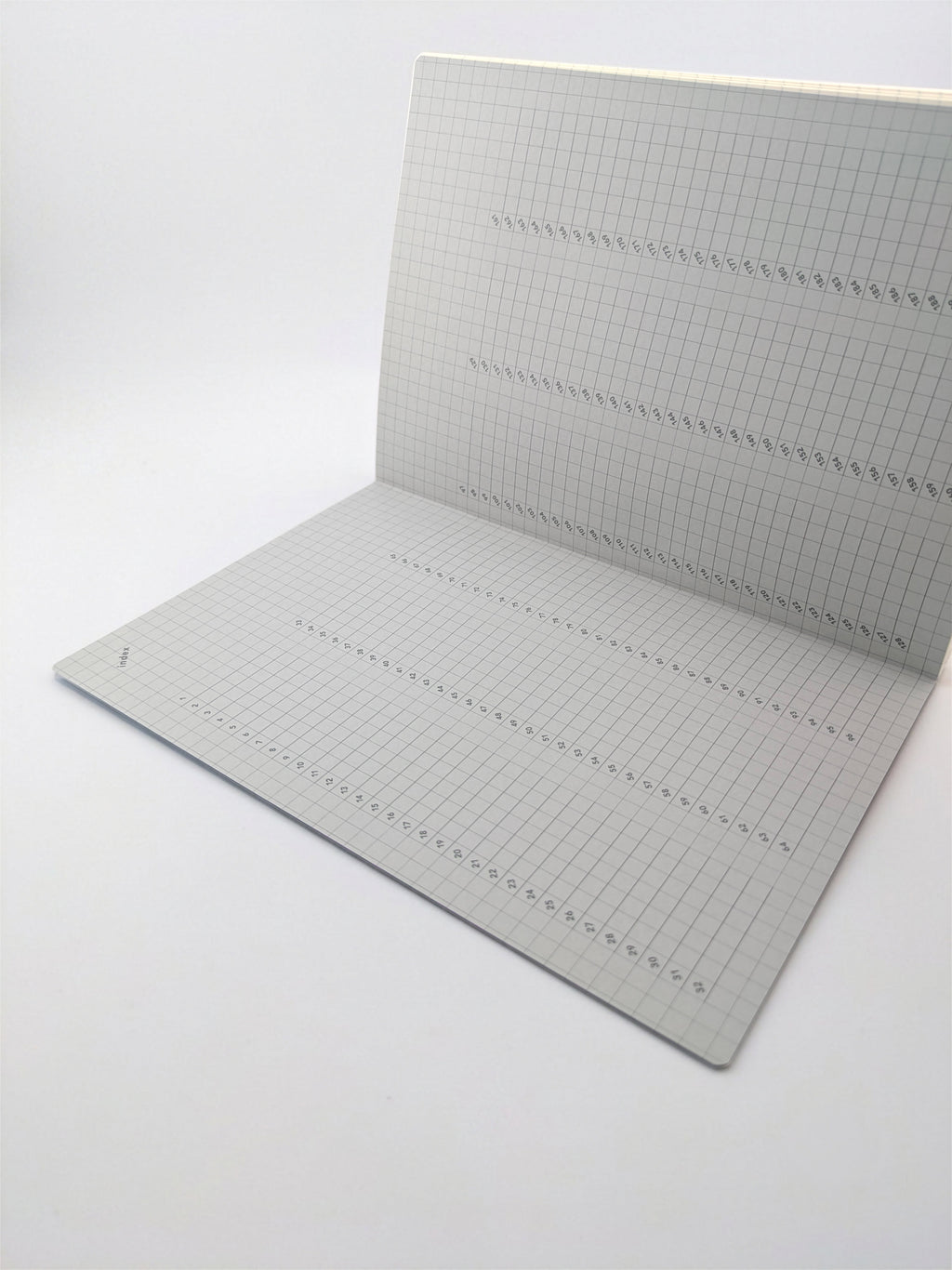 A square gray grid cutting mat with printed measurement markings and dashed guide lines, shown partially unfolded on a white background.