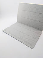 A square gray grid cutting mat with printed measurement markings and dashed guide lines, shown partially unfolded on a white background.
