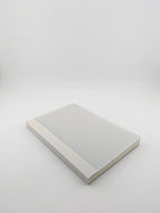 A minimalist hardcover book or notebook with a light gray cover and a beige spine, photographed on a seamless light gray studio background.