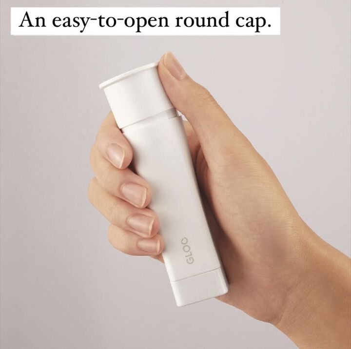 Hand holding white glue stick on light grey background.