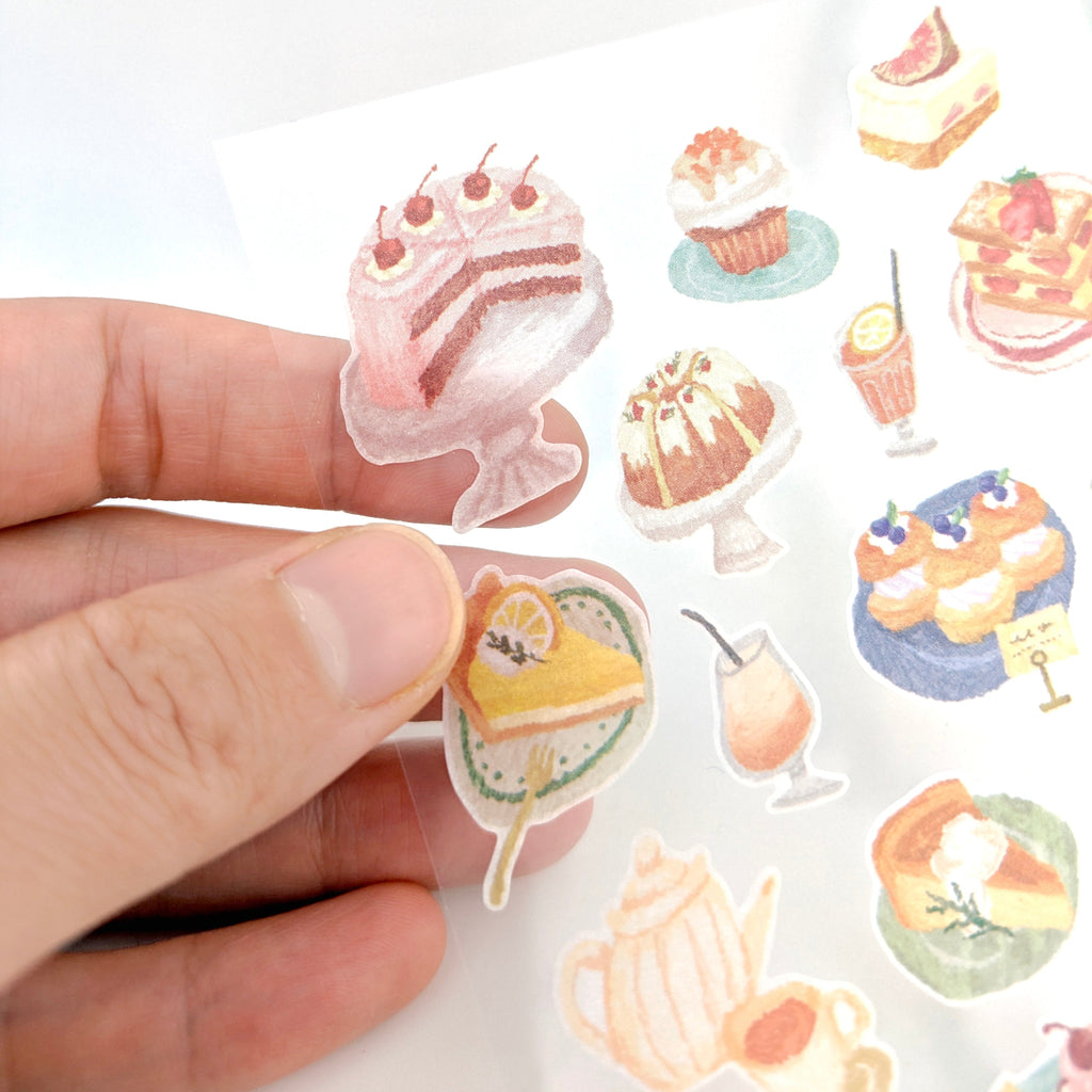Hand holding a sheet of dessert-themed stickers with various pastries and drinks.