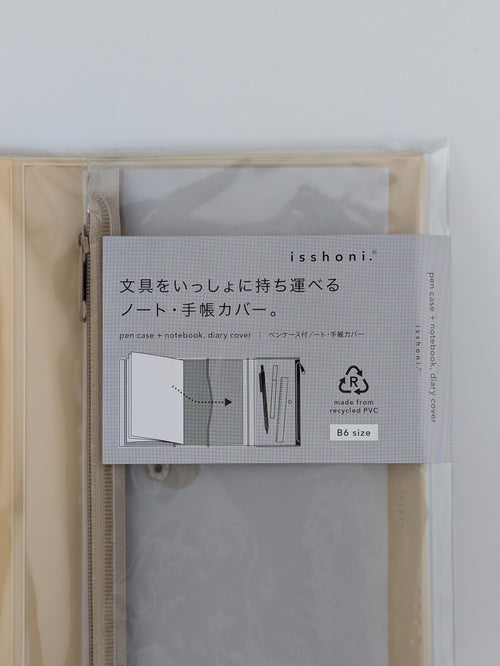 A translucent beige zippered notebook cover with a gray paper insert and a white product label that reads 'isshoni' and shows usage diagrams. The cover is photographed against a plain light gray background.