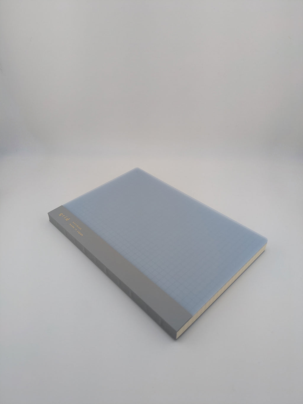 A hardcover notebook with a light blue grid-patterned cover and a gray spine, photographed on a seamless light gray background.
