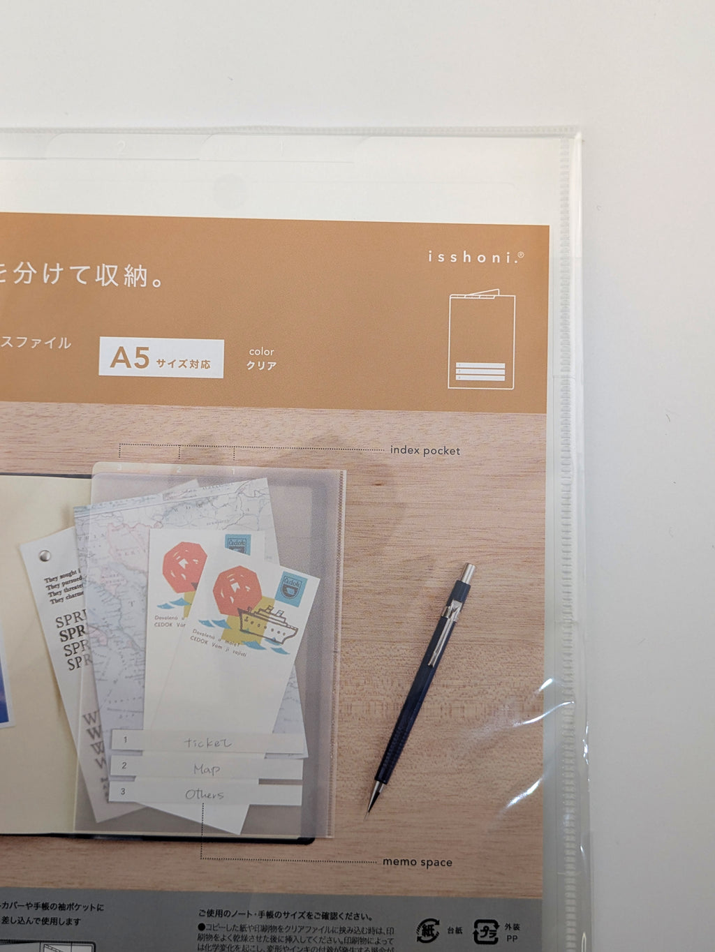 A clear plastic sleeve containing an Isshani A5 memo organizer with a tan and wood-grain design, shown with sample papers and a pen inside.