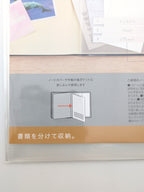 A close-up of a clear plastic document organizer sleeve containing a light wood folder with a gray paper insert featuring Japanese instructions and a tan banner at the bottom.