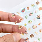 Finger with food-themed mini stickers applied on a white background.