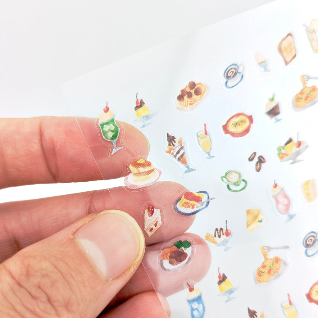 Hand holding mini food-themed stickers over white background.